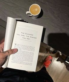 a person holding an open book next to a cup of coffee