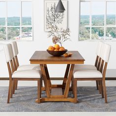 a wooden table topped with two white chairs next to a bowl of fruit on top of a rug