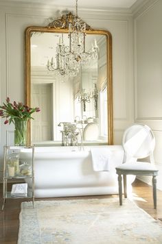 a white bath tub sitting under a large mirror next to a table with flowers on it