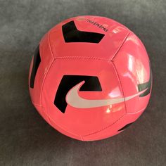 a pink nike soccer ball sitting on top of a gray carpeted floor next to a wall