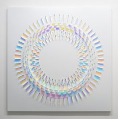 an art work with multiple colored lines in the shape of a circle on a white wall