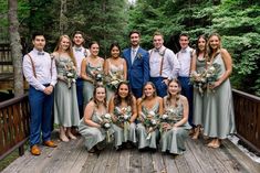 a group of people standing on top of a wooden bridge in front of some trees