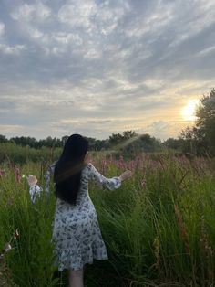 a woman standing in tall grass with her arms spread out to the sun behind her