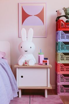 a white rabbit sitting on top of a dresser next to a pink bed in a bedroom