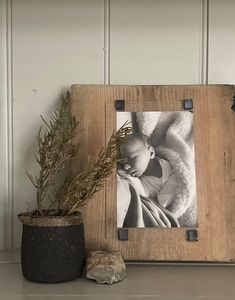 a wooden frame holding a baby's photo next to a potted plant