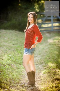 a woman in short shorts and cowboy boots posing for a photo on a dirt path