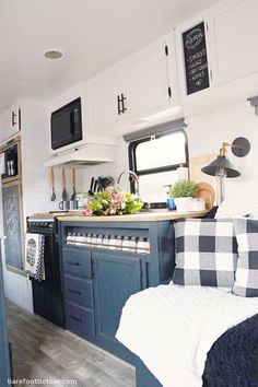 the interior of a camper with blue cabinets and plaid pillows on the bedding