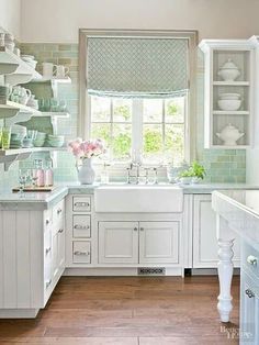 a kitchen with white cabinets and green tile backsplash, window above the sink