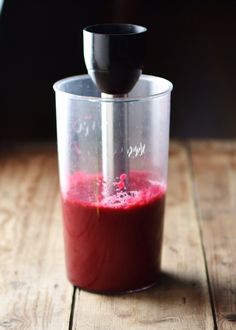 a blender filled with red liquid on top of a wooden table