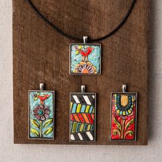 four square pendants with colorful designs on them sitting on a piece of brown wood