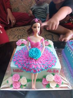 a birthday cake with a barbie doll on top and pink flowers in the middle, sitting on a table