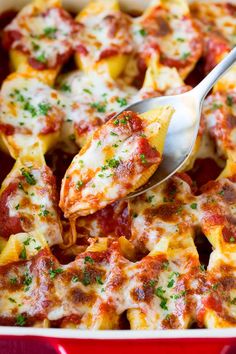 a red casserole dish filled with cheese and sauce, topped with a spoon