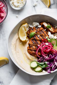 a bowl filled with chicken and vegetables on top of a white tablecloth next to sliced lemons