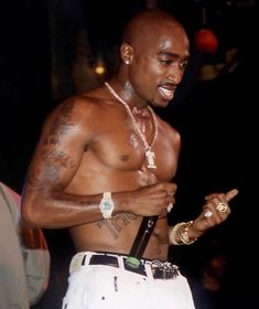 a shirtless man with tattoos on his chest holding a cell phone and wearing white pants