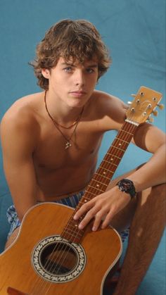 a shirtless young man holding an acoustic guitar