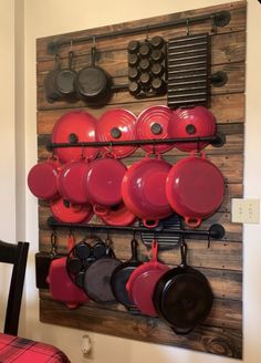 red pots and pans are hanging on the wall in front of a wooden rack