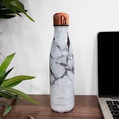 a white marbled bottle sitting on top of a wooden desk next to a laptop