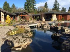 a house with a pond in front of it next to some rocks and trees on the other side