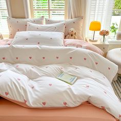 a bed with pink hearts on it in a bedroom next to a lamp and window