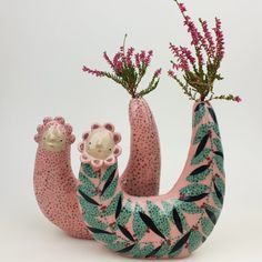 two pink and green stuffed animals with flowers in their hands, one holding the other's leg