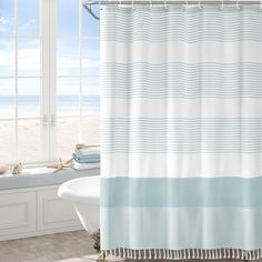 a bathroom with a bathtub, shower curtain and window overlooking the beach in front of it