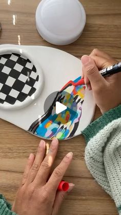 a woman is painting a black and white checkerboard design on a paper plate