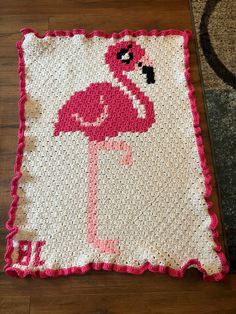 a crocheted pink flamingo pillow sitting on top of a wooden floor next to a rug