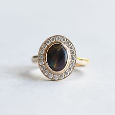 an oval shaped ring with a black stone surrounded by small white and clear diamonds on a plain surface