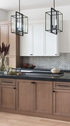 a kitchen with wooden cabinets and black counter tops, hanging lights over the island area