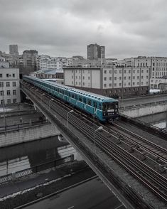 a blue train traveling through a city next to tall buildings on tracks and overpasss