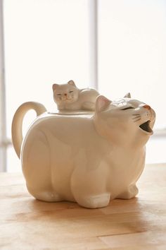 two white ceramic cats sitting on top of a wooden table next to each other and one has its mouth open