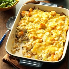 a casserole dish with meat and vegetables in it on a wooden table next to a bowl of green beans