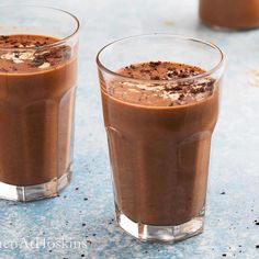 two glasses filled with chocolate pudding on top of a blue countertop next to each other