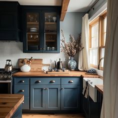 a kitchen with dark blue cabinets and wooden counter tops, along with white curtains on the window sill