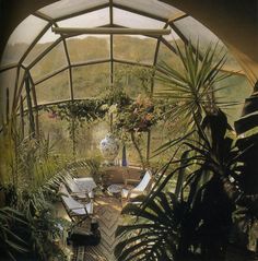 the inside of a greenhouse with lots of plants and chairs in it's center