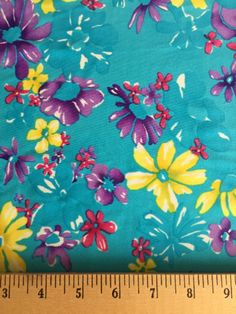 a ruler is next to a blue flowered fabric with yellow and purple flowers on it