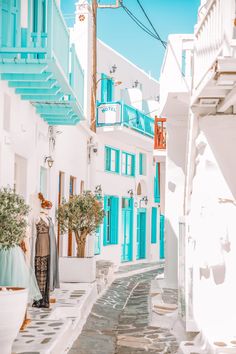 an alley way with white buildings and blue balconies on either side, in the daytime