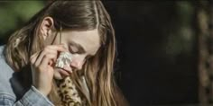 a woman with long hair talking on a cell phone while wearing a denim shirt and leopard print scarf