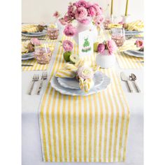 the table is set with yellow and white striped linens, silverware, and pink flowers