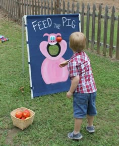 a young boy standing in front of a feed the pig sign