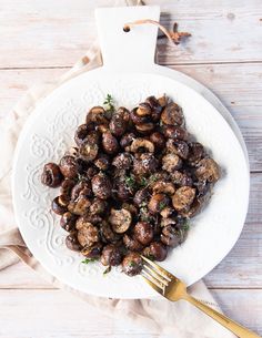 a white plate topped with cooked mushrooms next to a fork and napkin on top of a wooden table