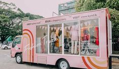 a pink food truck parked on the side of a road next to trees and buildings