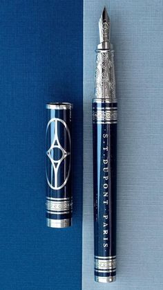 a pen sitting on top of a blue surface next to a metal container with an emblem