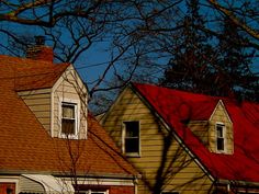 two houses with red roof tops and trees in the foreground, against a blue sky