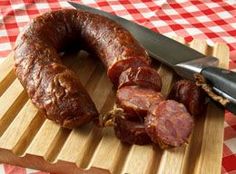 a knife and some sausages on a cutting board with a checkered table cloth