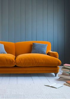 an orange couch sitting in front of a stack of books on top of a white floor