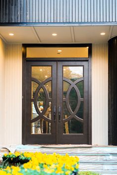 the front entrance to a building with two double doors and yellow flowers on the sidewalk