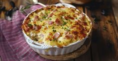 a casserole dish with ham and cheese in it on a wooden table next to bread