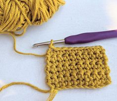 a crochet square with a purple handle next to it and a ball of yarn