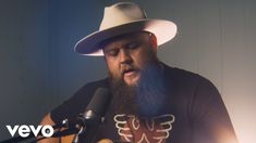 a man with a beard wearing a white hat and holding a guitar in front of a microphone